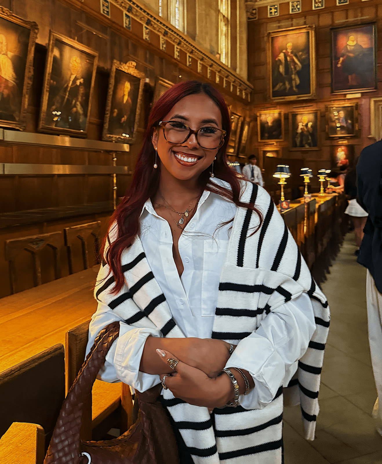 Melodi in a striped shirt and glasses inside a warmly lit restaurant